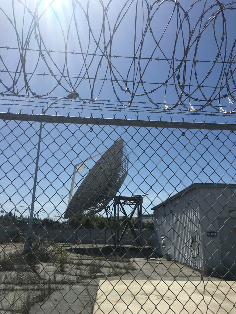 An old satellite is seen through fencing and barbed wire - Onizuka AFB