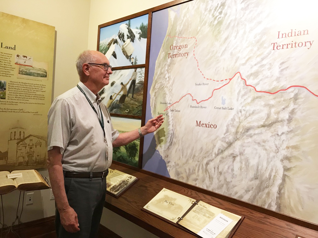 A docent points to a map and explains a caravan trek over the Rockies